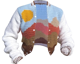 May include: A colorful, crocheted varsity jacket featuring a landscape design. The jacket has white sleeves and a button-up front. The body of the jacket showcases a sun, mountains, and sky in shades of blue, brown, and orange. The jacket is a unique, handmade piece.