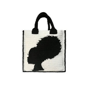 May include: A white crocheted tote bag with a black silhouette of a woman with an afro hairstyle.