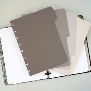 Może przedstawiać: Czarny notes w białe kropki z zestawem szarych, białych i jasnoszarych przegródek. Przegródki są zaprojektowane do dopasowania do planera z dyskami.