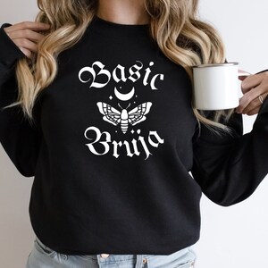 May include: Black sweatshirt with white text that reads "Basic Bruja" with a crescent moon and moth graphic.