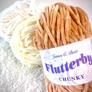 May include: Two skeins of yarn, one beige and one white. The beige skein is labeled "James C. Brett Flutterby Chunky".