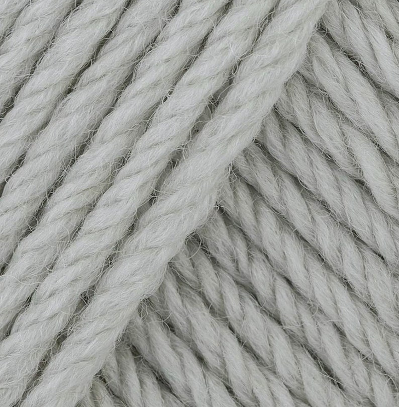 May include: Close-up of a skein of light gray yarn. The yarn is made of a soft, fluffy fiber and has a slightly textured surface.