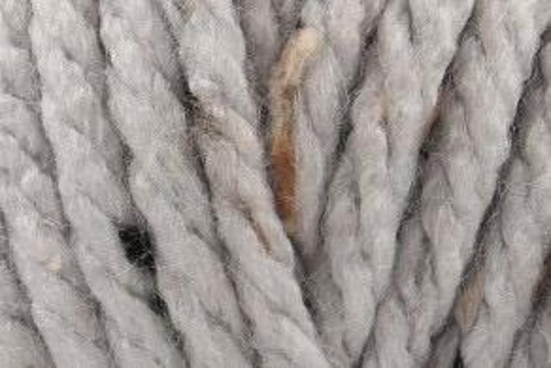 Peut inclure: Gros plan sur un fil de laine gris clair avec des taches brunes. Le fil est &eacute;pais et textur&eacute;, avec une apparence de corde.