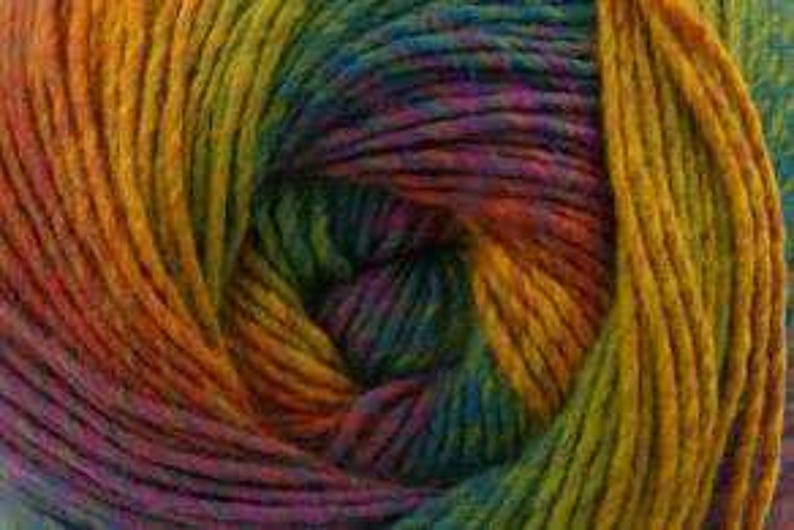 May include: Close-up of a skein of yarn with a vibrant rainbow color gradient. The yarn transitions from orange to yellow, green, blue, and purple. The yarn is tightly wound, showing the texture of the fibers.