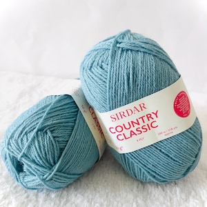 以下が含まれることがあります： 水色のSirdar Country Classic 4 Plyの毛糸玉が2つ。各玉にはブランド名、糸の種類、50gの重さが表示されています。ラベルには、糸の長さが約200メートルであることも記載されています。