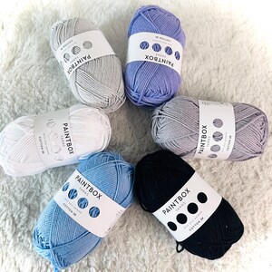 May include: Six balls of yarn in various colors, including white, light blue, dark blue, gray, and purple. Each ball has a label that says "Paintbox Yarns" and includes the text "Cotton DK".