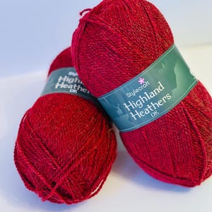 May include: Two balls of red yarn labeled "Stylecraft Highland Heathers DK"