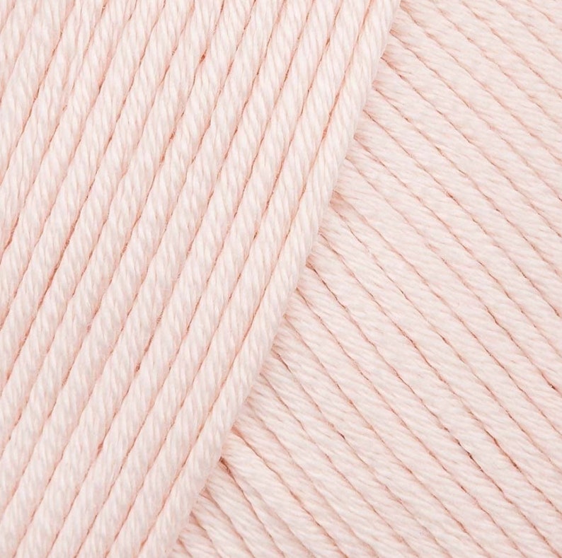 May include: Close-up of a soft, pale pink yarn. The yarn is made of cotton and is perfect for knitting or crocheting.