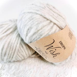 May include: Two skeins of DROPS Wish yarn in a light gray color. The yarn is a blend of baby alpaca, cotton, and wool. The label reads "DROPS Wish mix A super soft mix of Baby Alpaca, Puma, Cotton and Wool."