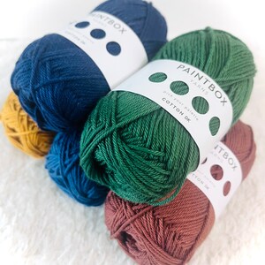 May include: Four balls of yarn in different colors: mustard yellow, navy blue, forest green, and terracotta. Each ball has a white label with the text "Paintbox Yarns" and "Pick your palette Cotton DK".