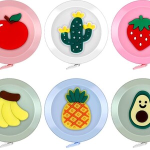 May include: Six colorful, round, retractable tape measures with different fruit and plant designs. The designs include a red apple, a green cactus, a red strawberry, a yellow banana, a yellow pineapple, and a green avocado.