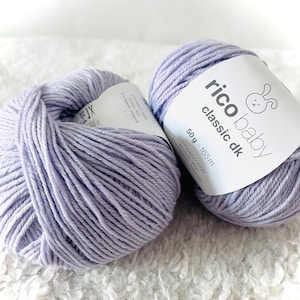 May include: Two balls of lavender-colored yarn. One ball has a label that reads "rico baby classic dk" with a bunny logo. The label also indicates the yarn is 50g and 165m. The yarn is 50% Polyacryl/Acrylic and 50% Polyamid/Polyamide.