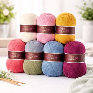 May include: A collection of colorful yarn balls in various shades, including pink, yellow, blue, and purple. Each ball has a brown label with the text "Special Dhi". Knitting needles and a green cloth are in the foreground.