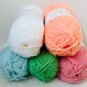 May include: Five balls of yarn in different colors: white, peach, light blue, green, and pink. The yarn is arranged in a pyramid shape.