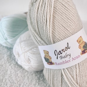 May include: Three balls of yarn in white, light blue, and beige. The beige ball has a label that reads "Jarol Baby Rambler Aran".