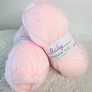 May include: Two balls of pink yarn with silver glitter. The yarn is labelled "Baby Shimmer D.K. Superwash Machine Washable."