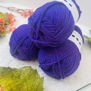 Op de afbeelding: Drie bollen paarse garen, elk met een wit label waarop "Knitbox" staat.