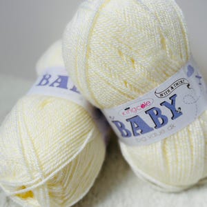 May include: Two skeins of pale yellow baby yarn. The yarn is tightly wound and labelled with the text "BABY" and "big value dk". The yarn is suitable for knitting or crocheting baby clothes and blankets.