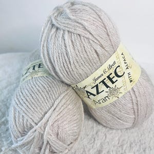 May include: Two skeins of light beige yarn labeled "Aztec Aran with Alpaca" by James C. Brett.