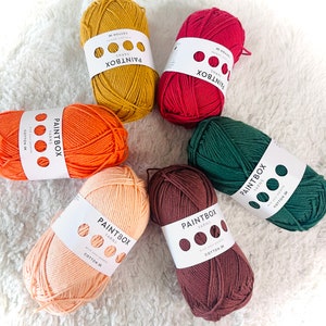 May include: Six balls of yarn in various colors, including orange, red, green, brown, and peach. Each ball has a label that reads "Paintbox Yarns" and includes the text "Cotton DK".
