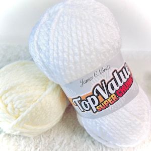 Puede incluir: Dos ovillos de hilo blanco, uno es un hilo super grueso con una etiqueta que dice "Top Value Super Chunky" y el otro es un hilo más ligero.