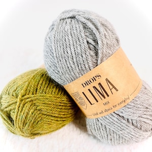 Può includere: Due gomitoli di lana, uno grigio e uno verde, con un'etichetta marrone che recita "DROPS LIMA MIX Lana e alpaca per tutti i giorni!"