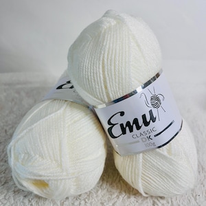 May include: Two skeins of off-white Emu Classic DK yarn, each labeled 100g. The yarn is tightly wound, showing a soft, textured surface. The labels feature the Emu logo with a stylized bird and the text "CLASSIC DK".
