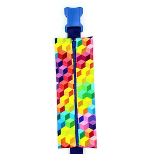 Peut inclure: Une pochette zippée colorée avec un motif géométrique de cubes dans des tons de rouge, orange, jaune, vert, bleu et violet. La pochette est dotée d'un clip en plastique bleu et d'une sangle bleu marine.
