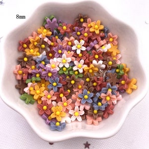 Peut inclure: Un bol rempli de petites décorations florales en résine colorées. Les fleurs mesurent environ 8 mm et sont disponibles dans une variété de couleurs, notamment le rose, le violet, le jaune, l'orange et le vert.