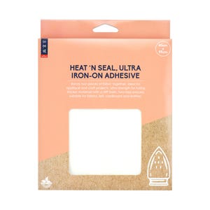 Puede incluir: Un paquete de Heat 'n Seal Ultra Iron-On Adhesive, de color melocotón y beige. El texto "HEAT 'N SEAL, ULTRA IRON-ON ADHESIVE" es visible. Dimensiones: 45 cm x 99 cm. Un cuadrado blanco es visible en el centro del paquete.