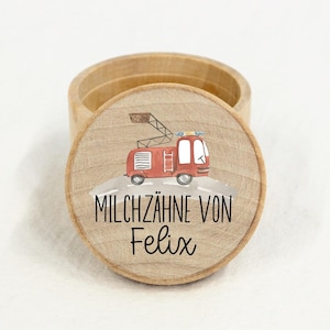 Könnte beinhalten: Eine Holzkiste mit einem runden Deckel. Der Deckel hat eine Aquarell-Illustration eines roten Feuerwehrautos und den Text "MILCHZÄHNE VON Felix".