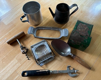 May include: A collection of vintage kitchen tools and utensils, including a metal egg slicer, a wooden handled corkscrew, a metal butter cutter, a metal measuring cup, a metal scoop, a green metal box, and a can opener.