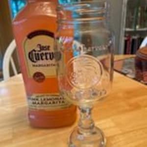 May include: A clear glass mason jar with a handle, etched with a design of a Native American head, next to a pink bottle of Jose Cuervo 'Original'  Margarita mix.