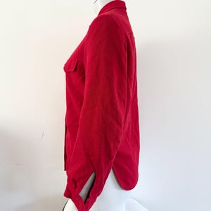May include: A solid red button-down shirt with long sleeves and a collared neckline. The shirt has a single chest pocket and a split cuff detail. The fabric appears to be a soft, textured material.