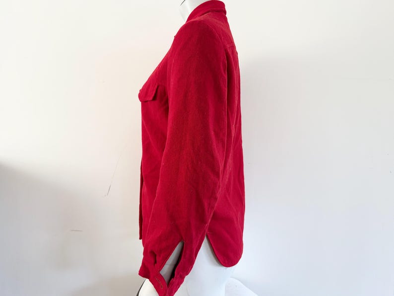 May include: A solid red button-down shirt with long sleeves and a collared neckline. The shirt has a single chest pocket and a split cuff detail. The fabric appears to be a soft, textured material.