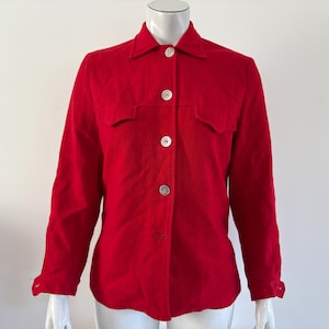 May include: A bright red button-down shirt with two chest pockets and long sleeves. The shirt has a classic collar and is fastened with four silver buttons. The garment is displayed on a mannequin.