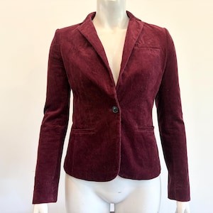 May include: A burgundy blazer with a single-button closure, notched lapels, and two front pockets. The jacket is made of a soft, velvety material. The blazer is displayed on a mannequin.