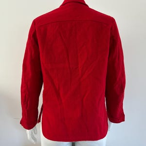 May include: A vibrant red long-sleeved shirt. The shirt features a classic collar, buttoned cuffs, and a button-down front. The back of the shirt is visible, showcasing the tailored design and the rich color of the fabric. The shirt is displayed on a mannequin.