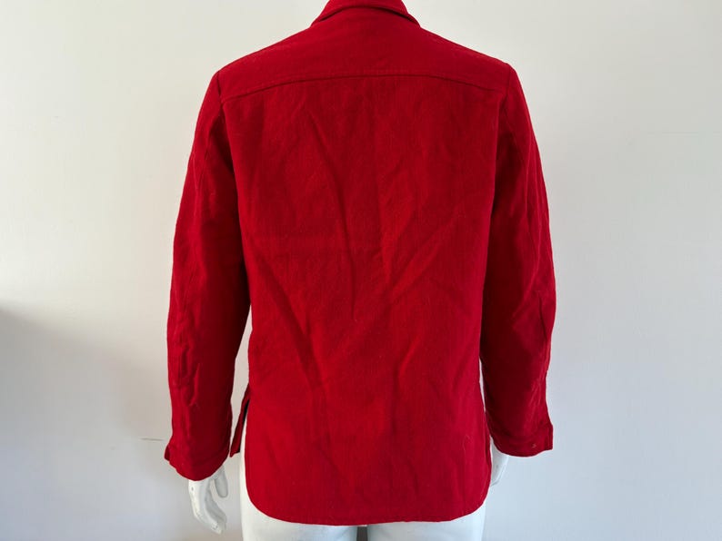 May include: A vibrant red long-sleeved shirt. The shirt features a classic collar, buttoned cuffs, and a button-down front. The back of the shirt is visible, showcasing the tailored design and the rich color of the fabric. The shirt is displayed on a mannequin.