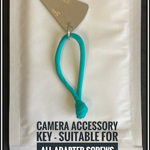 May include: A silver camera accessory key with a 2 mm slot, attached to a turquoise lanyard. The key is labelled "MI-KEE". The text on the image reads "CAMERA ACCESSORY KEY - SUITABLE FOR ALL ADAPTER SCREWS WITH A 2MM SLOT - THE PERFECT TOOL FOR YOUR CAMERA EQUIPMENT."