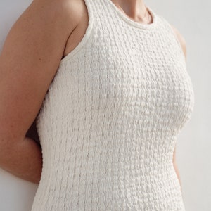 Op de afbeelding: Een witte, mouwloze jurk met een textuur van een wafel. De jurk is strak en heeft een eenvoudig, elegant ontwerp.