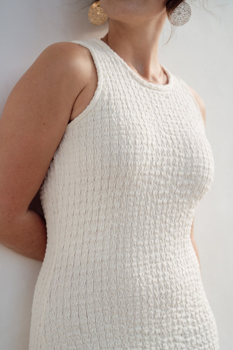 Op de afbeelding: Een witte, mouwloze jurk met een textuur van een wafel. De jurk is strak en heeft een eenvoudig, elegant ontwerp.