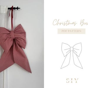 Op de afbeelding: Een grote, rood-witte geruite kerststrik die aan een zwarte stang hangt. De strik is gemaakt van stof en heeft lange, vloeiende uiteinden. De afbeelding bevat ook de tekst "Christmas Bow PDF Pattern".