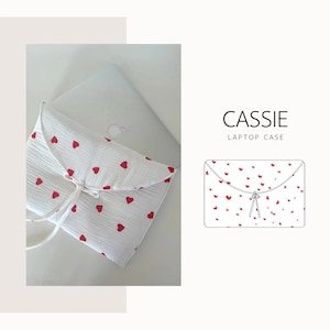 May include: White laptop case patterned with small red hearts. The case has a drawstring closure and is made from a soft, textured material. The text "CASSIE LAPTOP CASE" is displayed on the right.