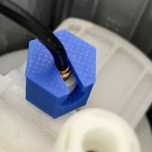 以下が含まれることがあります： 黒いワイヤーが通っている青い六角形の接続部のクローズアップ。接続部は白いプラスチックパイプに取り付けられています。