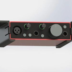 Könnte beinhalten: Ein schwarzes Audio-Interface mit roten Akzenten und zwei Knöpfen. Das Interface verfügt über einen Mikrofoneingang, einen Kopfhörerausgang und weitere Anschlüsse.
