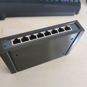 Op de afbeelding: Een zwarte 8-poorts netwerkswitch met RJ-45-connectoren.