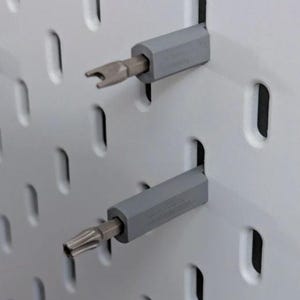 Könnte beinhalten: Zwei graue magnetische Schraubendreherhalter mit befestigten Schraubendreherbits aus Metall. Die Halter sind an einer weißen Lochwand befestigt.