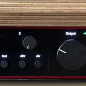 Pode incluir: Interface de áudio Scarlett Solo preta com acabamento vermelho, com botões, controles e conectores de entrada/saída. O dispositivo é montado sob uma superfície de madeira. O texto "Scarlett Solo" é visível.