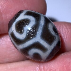 Puede incluir: Una cuenta de ágata negra y blanca con un patrón de espiral. La cuenta es de forma ovalada y tiene una superficie lisa y pulida.